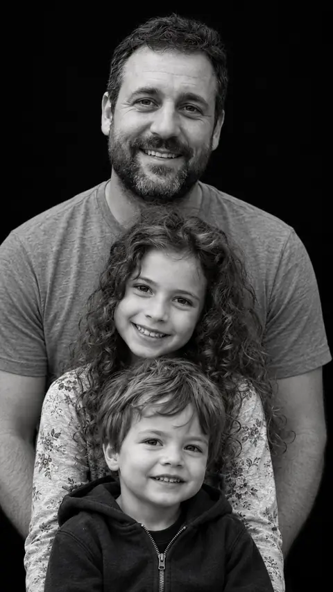 The same father as a stacked monochrome studio portrait, his curly-haired daughter in front of him and his son at the front, on a black background