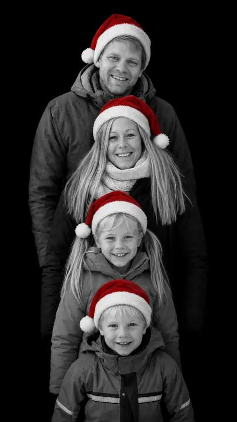 A family of four in winter coats in a stacked monochrome studio portrait, all four wearing red Santa hats